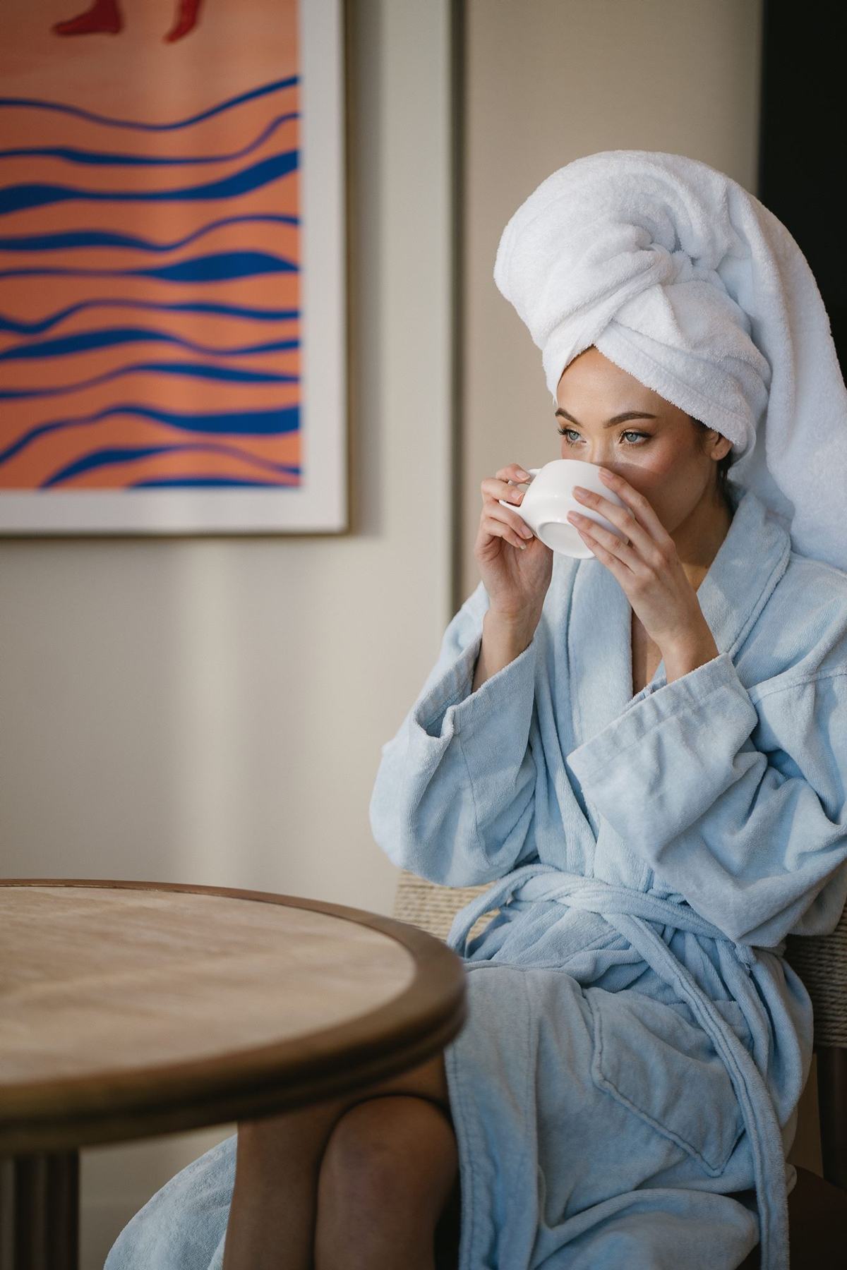 A guest in a robe with a coffee in her room